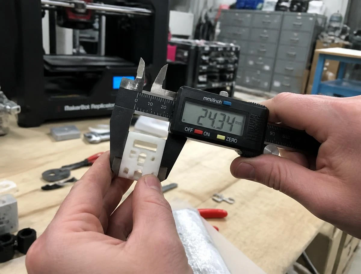 An engineer measuring a 3D printed prototype with digital calipers